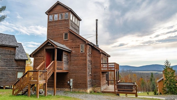 Una cabaña de madera con una torre central, un porche y vistas del paisaje circundante.