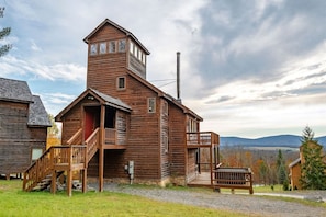A wooden cabin with a central tower, a porch, and a view of the surrounding landscape.