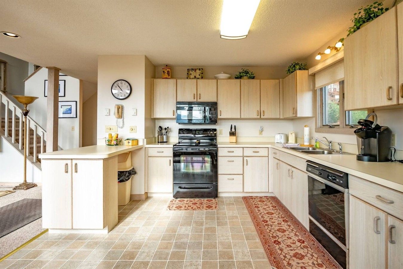 Una cocina moderna con armarios de madera clara, una estufa negra y un reloj en la pared.