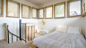 Un dormitorio con cama, mesita de noche, lámpara, ventana con persianas y barandilla de madera.