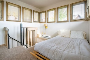 Un dormitorio con cama, mesita de noche, lámpara, ventana con persianas y barandilla de madera.