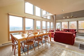 Une pièce spacieuse comprenant une table à manger, des chaises et un canapé rouge. De grandes fenêtres offrent une vue sur l’extérieur.
