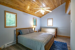 A bedroom with a wooden ceiling, a bed with a quilted bedspread, two bedside tables with lamps, and a window with blinds. - Robin`s Perch - 318 Northpoint Way (Davis)