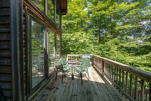 Un terrazzo in legno con tavolo e sedie, circondato da una ringhiera di legno, con vista su una fitta foresta.