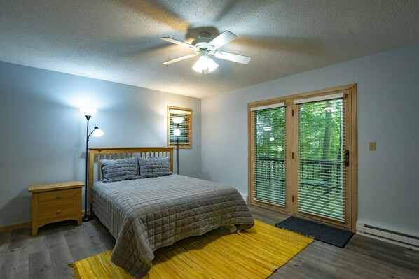 A bedroom with a bed, bedside lamp, ceiling fan, and a view through a window with blinds. - Robin`s Perch - 318 Northpoint Way (Davis)