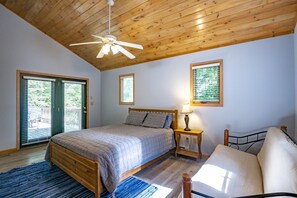 Una camera da letto con soffitto in legno, un letto con testiera, un comodino con una lampada, una finestra con persiane e vista sull'esterno.
