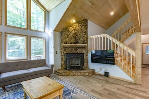 Una sala de estar con chimenea de piedra, un televisor grande montado en la pared, una escalera de madera y un sofá.