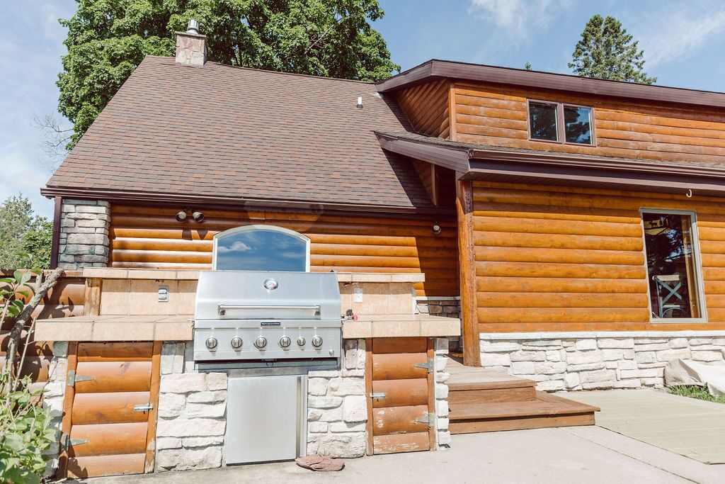 Une cabane en rondins avec des fondations en pierre, un grand barbecue et une cheminée.
