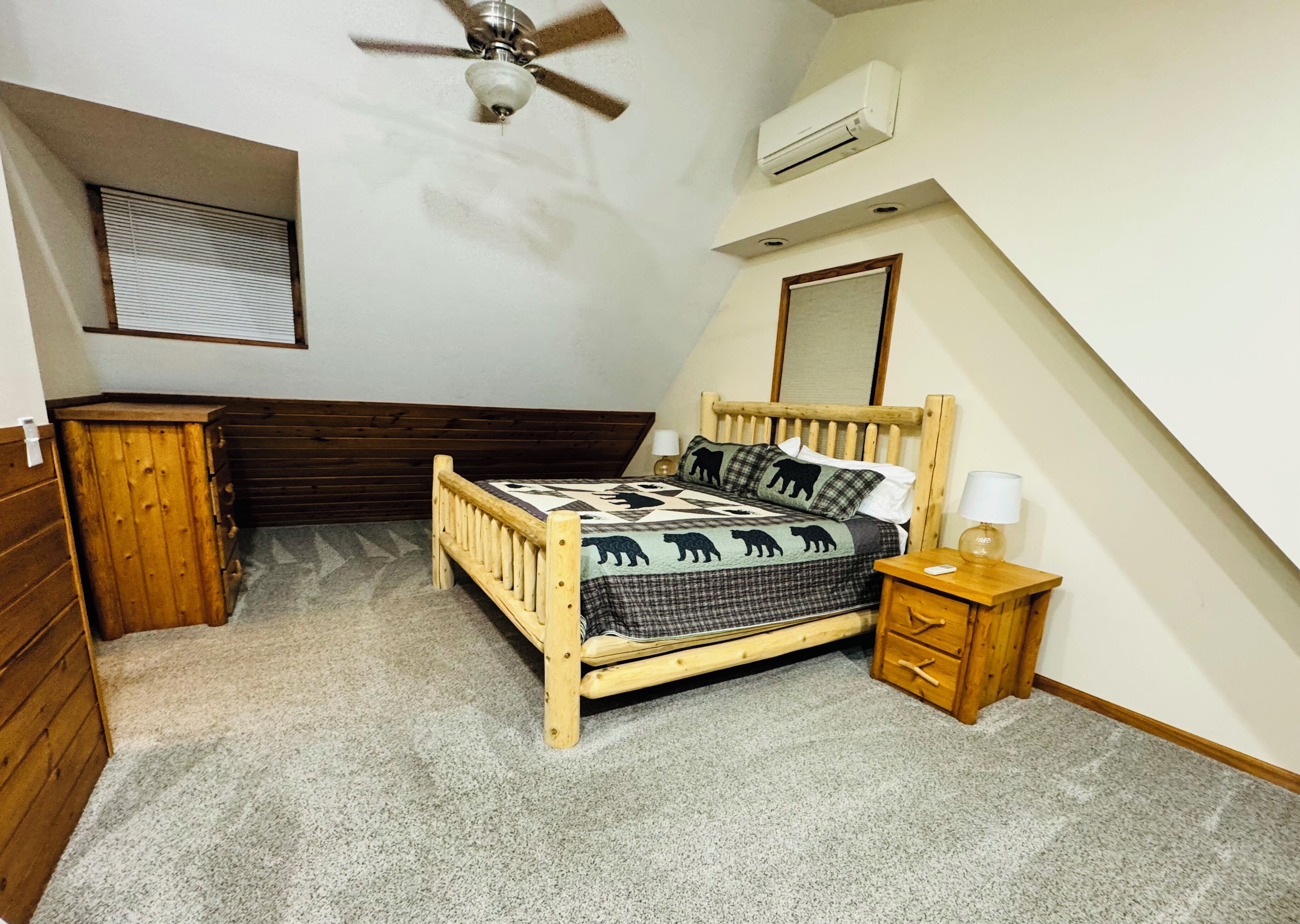 Ein Schlafzimmer mit einem hölzernen Bett, einem Nachttisch, einer Kommode, einem Deckenventilator und einer Klimaanlage.