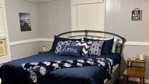 Een slaapkamer met een bed, twee nachtkastjes, een houten stoel, een vloerkleed, een schilderij aan de muur, en een bord met daarop 'No Wake Zone'.