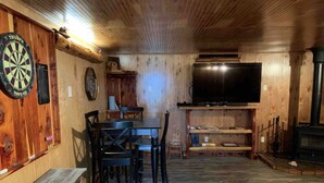 Een knus vertrek met houten inrichting, een dartbord, een flatscreen televisie, een open haard en een tafel met stoelen.