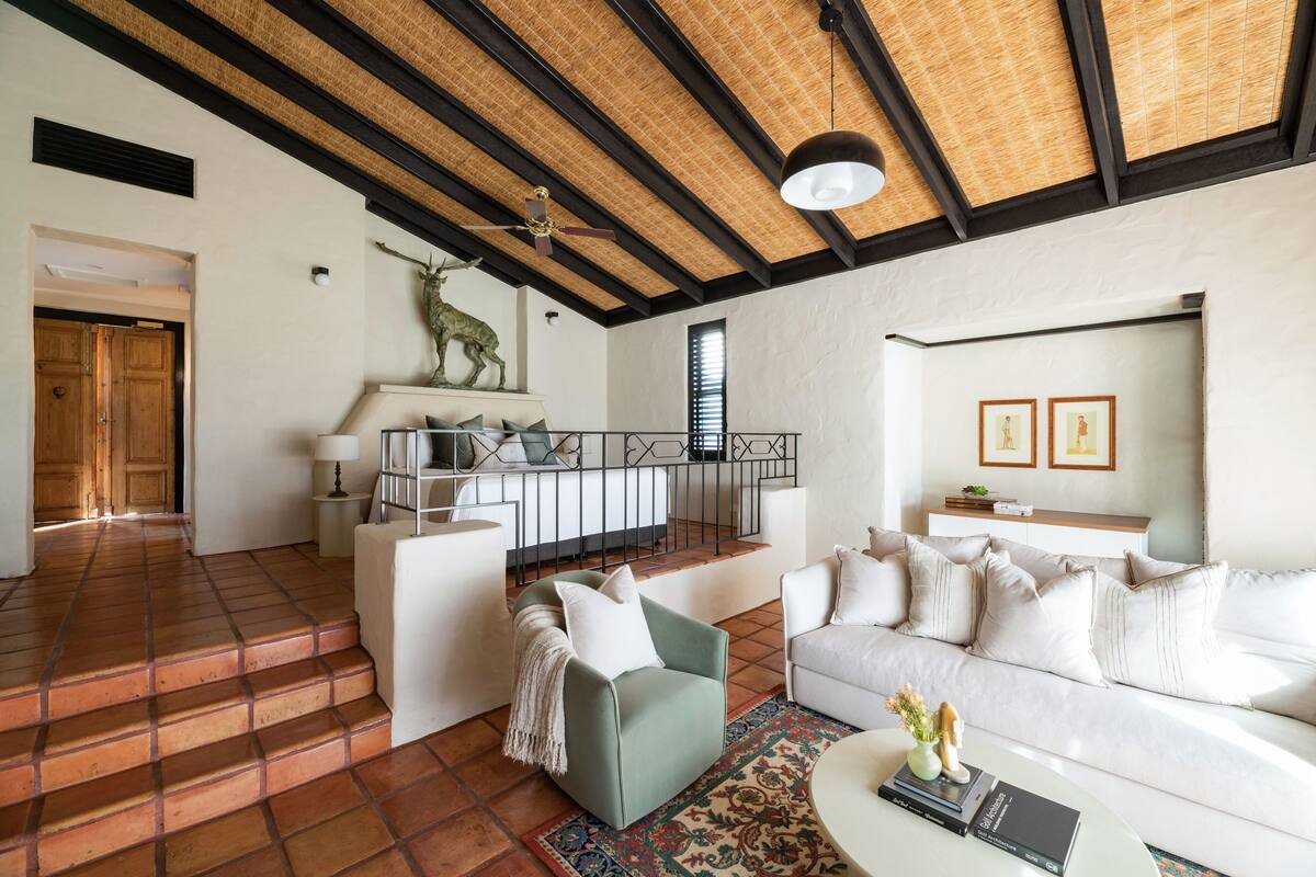A spacious living area with a high ceiling, a fireplace, a sofa, a coffee table, and a staircase leading to another room.