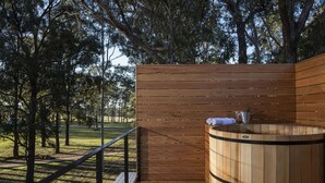 A wooden sauna with a bench, surrounded by a wooden deck and a railing, set in a wooded area. - Tower Lodge (Pokolbin)
