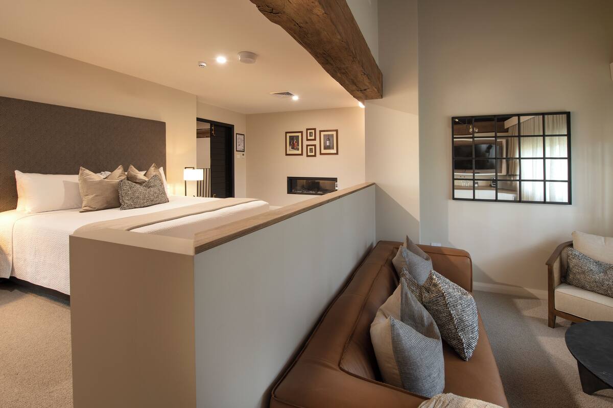 A modern hotel room with a large bed, a seating area, and a fireplace.