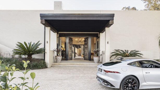 A modern building with a paved entrance, a parked sports car, and potted plants. - Tower Lodge (Pokolbin)