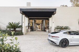 Un edificio moderno con entrada pavimentada, un coche deportivo estacionado y plantas en macetas.