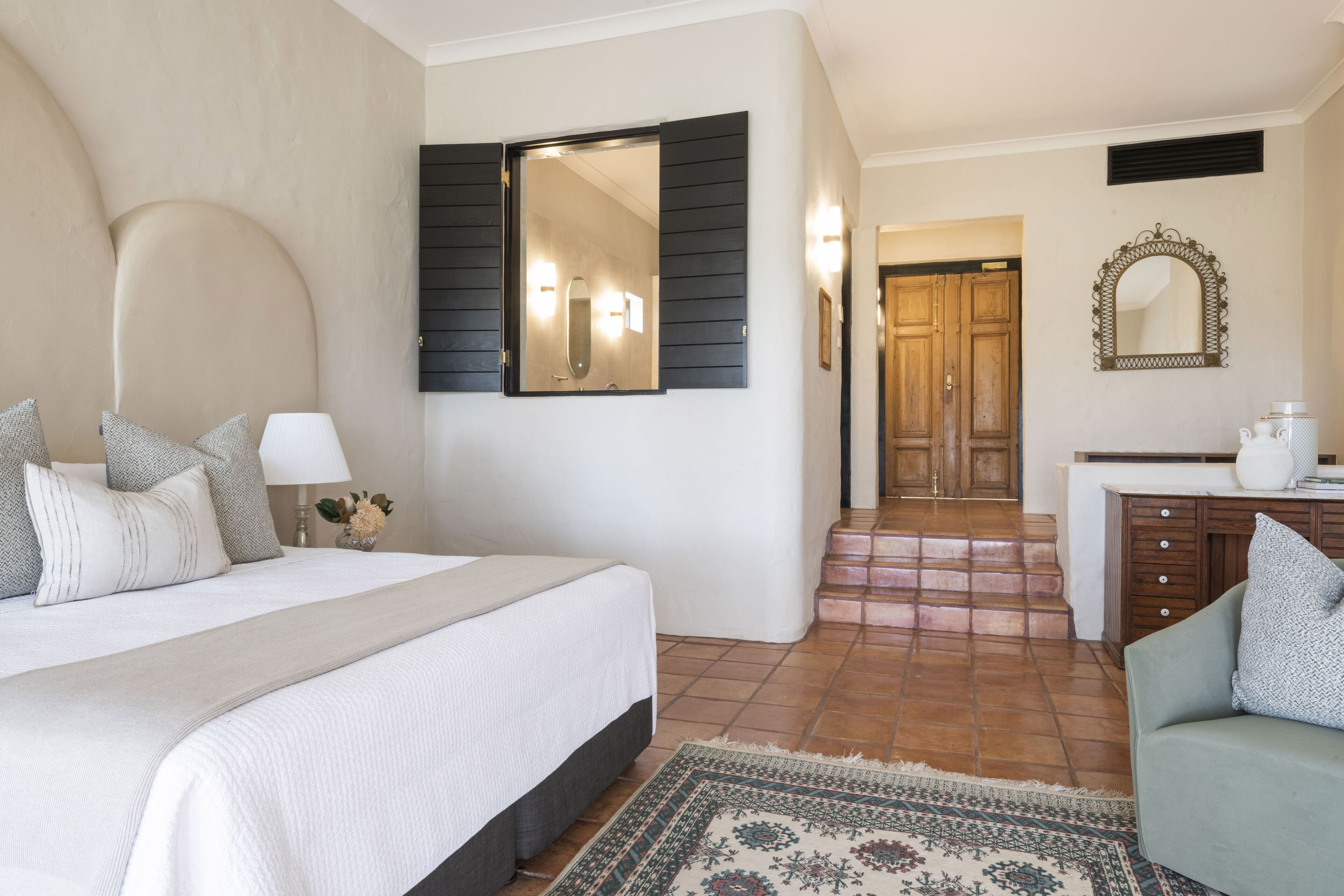 A bedroom with a bed, bedside table, lamp, and a large mirror.