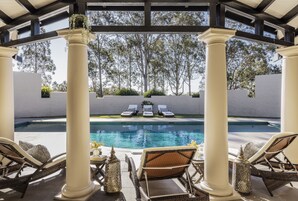 Uma área à beira da piscina com espreguiçadeiras, uma pérgola e vista para a piscina.