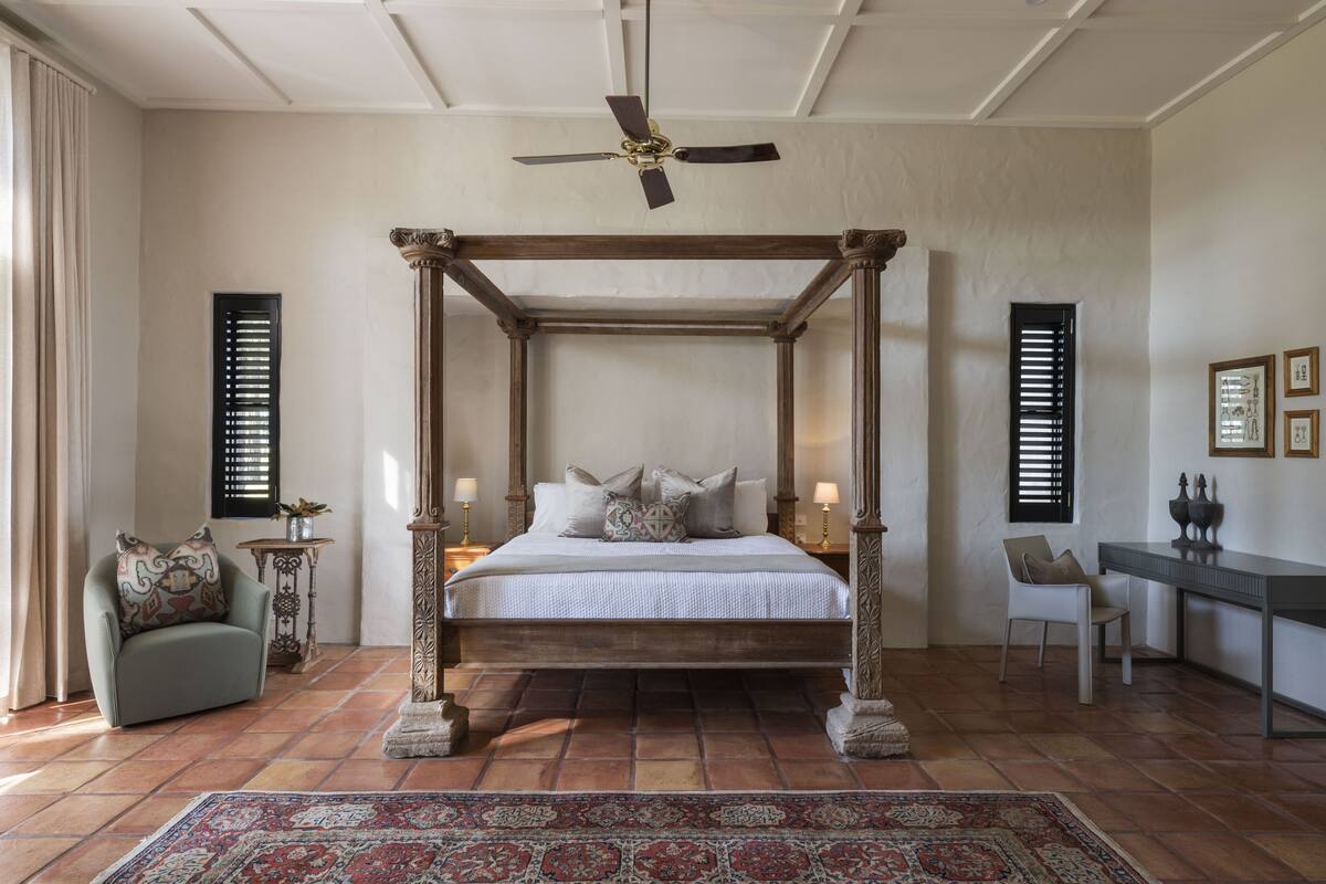 A bedroom with a four-poster bed, a desk, and two chairs.