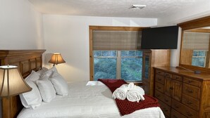 Ein ordentlich bezogenes Bett mit weißen Leinen, einem Holzkopfende, einer Nachttischlampe und einer roten Tagesdecke.