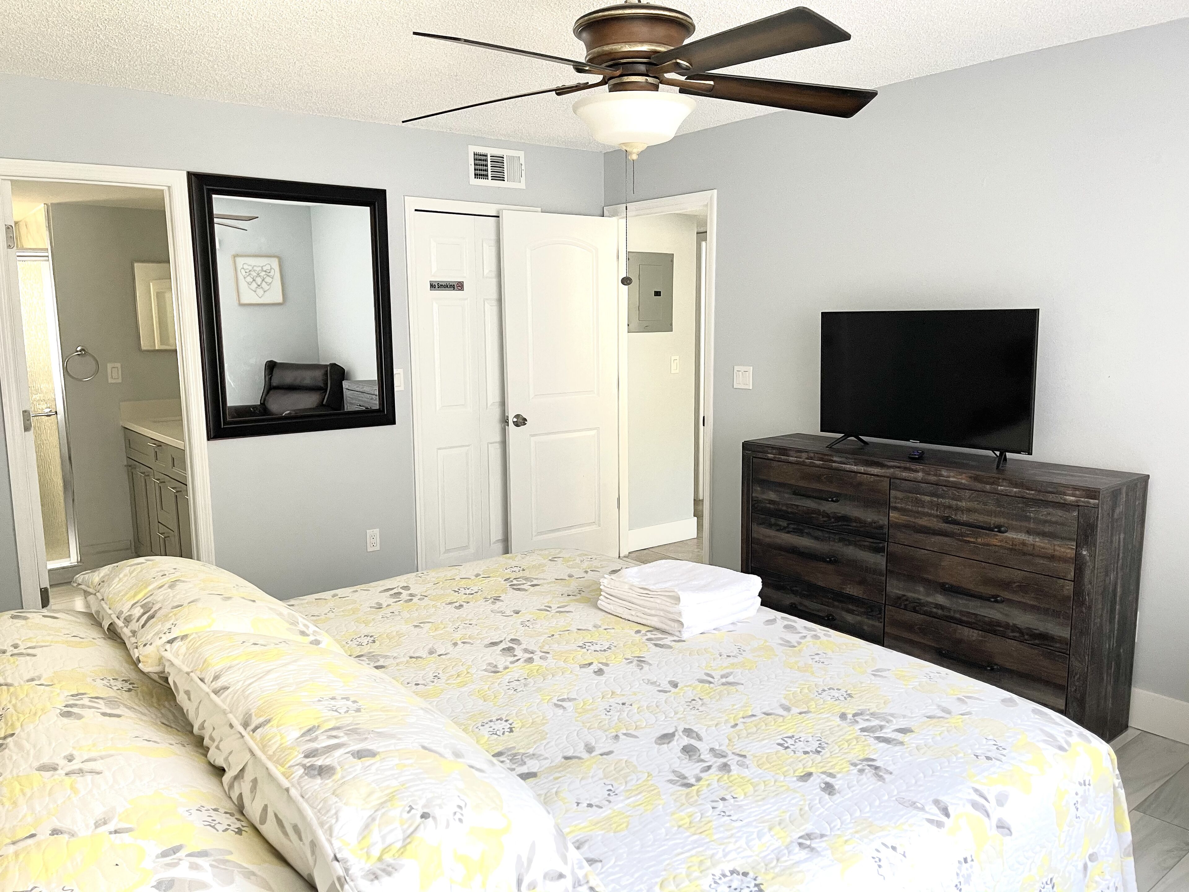 A bedroom with a bed, dresser, TV, and a ceiling fan.