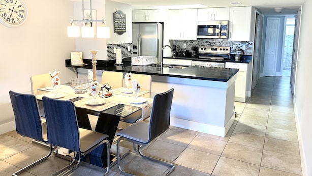 Een moderne keuken met witte kasten, een centraal eiland, roestvrijstalen apparatuur en een eethoek met blauwe stoelen.