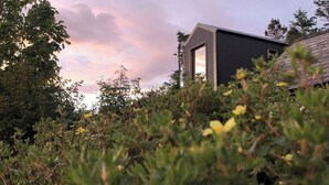 A building with a dark facade and a large window, surrounded by dense vegetation and flowers. - Tiny Home in Isle of Skye - Pet Friendly (Isle of Skye)