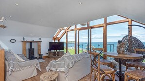 Ein gemütlicher Wohnbereich mit Fernseher, Sofa und Holzmöbeln, mit Blick auf eine malerische Meereslandschaft.