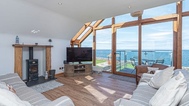 Ein Wohnzimmer mit Fernseher, Holzmöbeln und einem großen Fenster mit Meerblick.