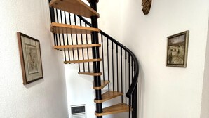 Eine Wendeltreppe mit Holzsitzstufen und schwarzen Metallgeländern, begleitet von gerahmten Bildern an den Wänden.
