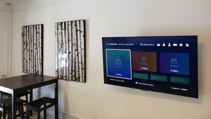 A room with a flat-screen TV mounted on the wall displaying a streaming service interface. - Beautiful 2BR Suite just off Main St, Picton, near Sandbanks (Prince Edward)