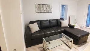 A modern living room with a black leather sofa, a glass coffee table, and a minimalist wall art piece. - Beautiful 2BR Suite just off Main St, Picton, near Sandbanks (Prince Edward)