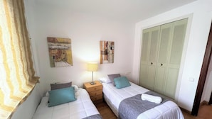 A bedroom with two beds, a nightstand, a lamp, and a wardrobe with louvered doors. - Arquus III Beach Salou, with swimming pool (Salou)