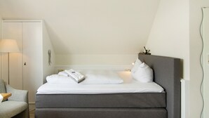 Et soveværelse med seng, stol, lampe og et spejl på væggen.