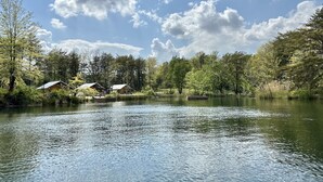 Una cabaña junto al lago con un muelle, rodeada de un bosque frondoso y cielos despejados.
