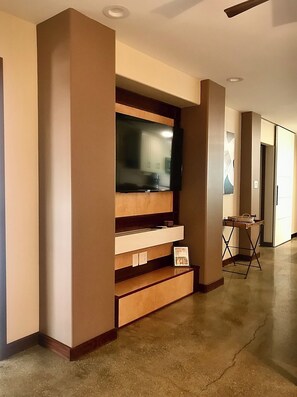A modern living room with a flat-screen TV mounted on a wooden cabinet, a small table with a basket, and a framed photo on the lower shelf.