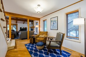 A cozy living room with a wooden staircase, a television, and a framed picture of a lake.