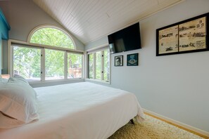 A bedroom with a large bed, multiple windows, a flat-screen TV, and framed pictures on the wall.