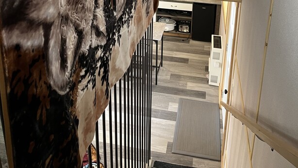 Ein modernes Interieur mit einem großen abstrakten Gemälde an der Wand, einer Küchenzeile mit Geräten und einer Treppe, die zu einer weiteren Ebene führt.