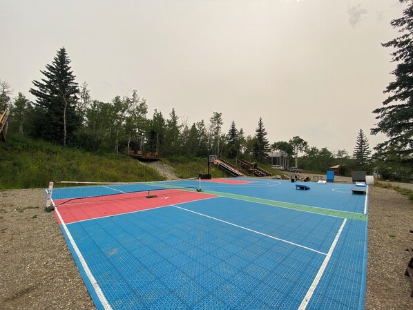 Un campo sportivo all'aperto con superficie blu e rossa, circondato da alberi e un piccolo edificio.