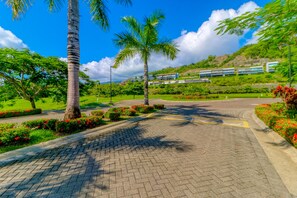 A paved pathway leading to a modern building complex with a landscaped garden and palm trees.
