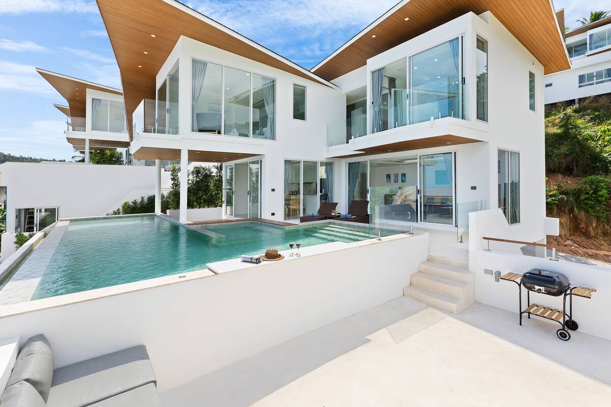 A modern house with a swimming pool, outdoor seating, and a barbecue area.