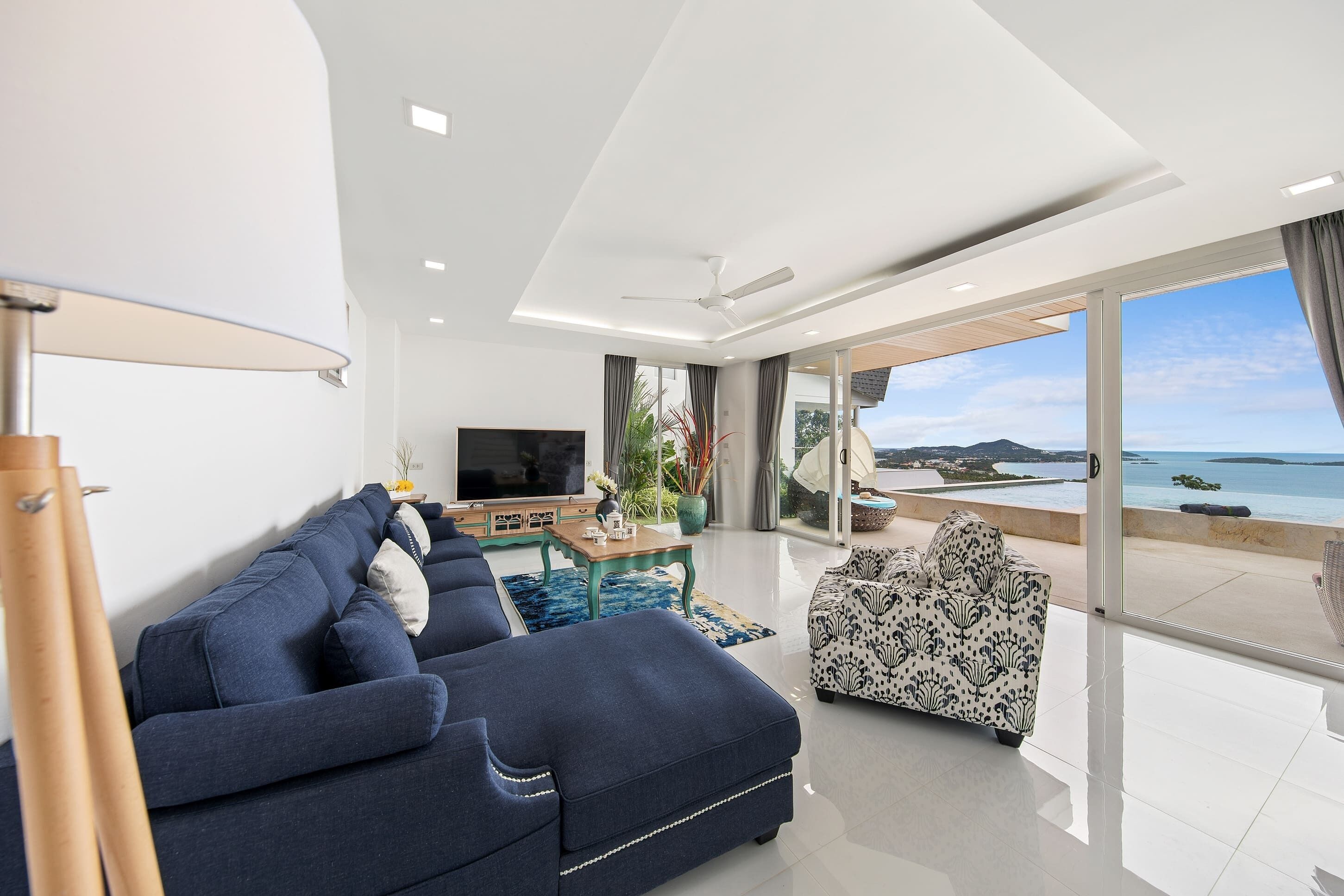 Un saló modern amb un sofà, una butaca estampada, una televisió i vista al mar.