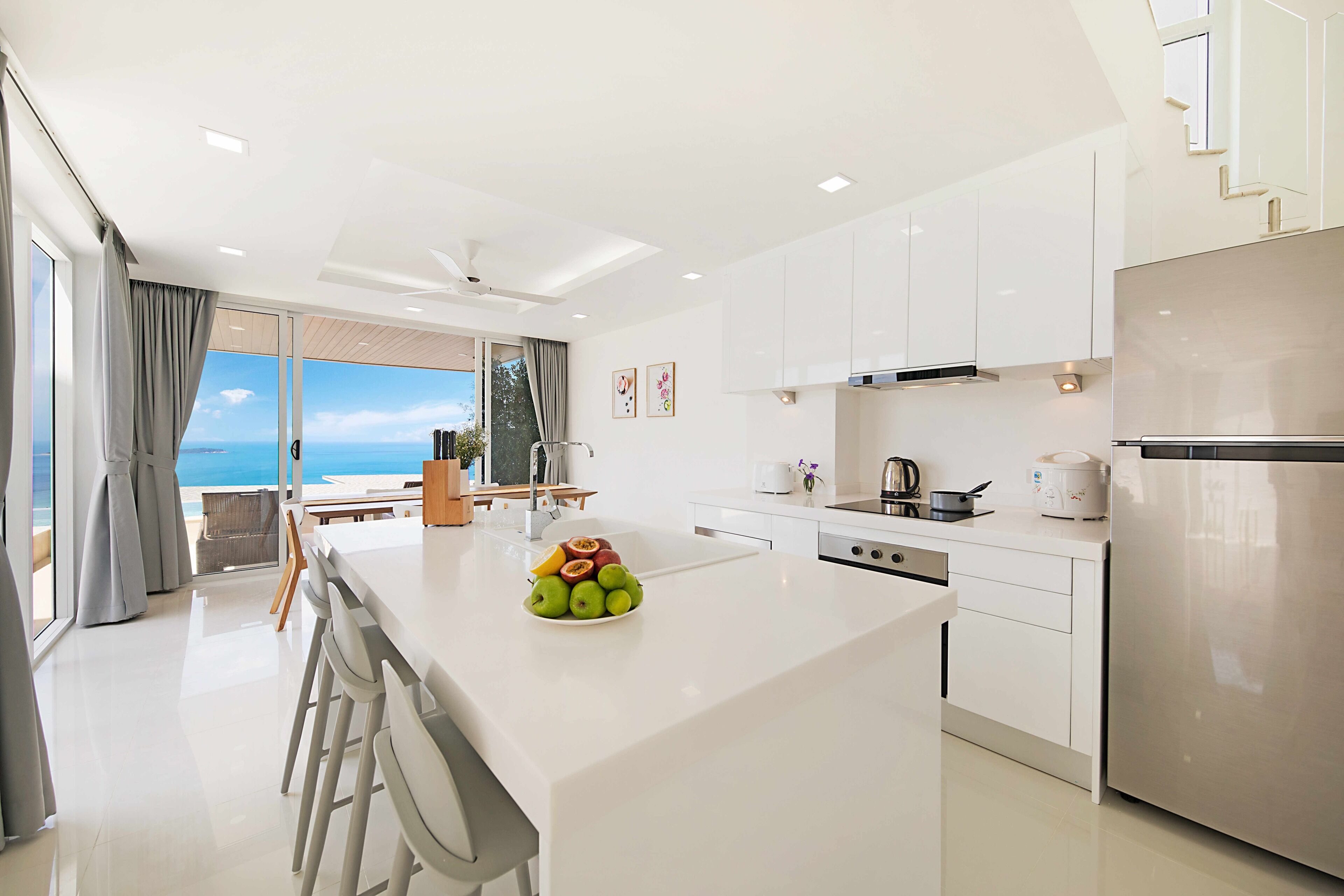 Una cocina moderna con una isla central, muebles blancos y un refrigerador de acero inoxidable.