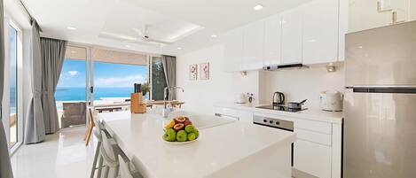 Una cocina moderna con una isla central, muebles blancos y un refrigerador de acero inoxidable.