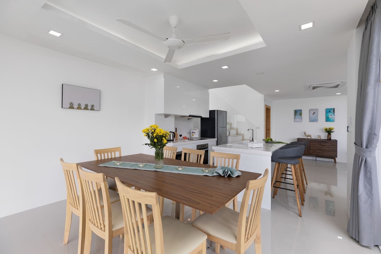 Une cuisine moderne avec des meubles blancs, un îlot central et un coin repas comprenant des chaises et une table en bois.
