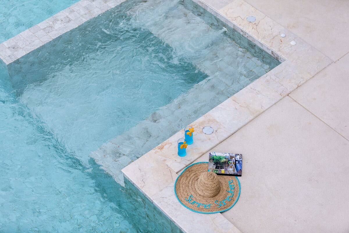 A pool with clear water, a sun lounger, and a drink on the edge.