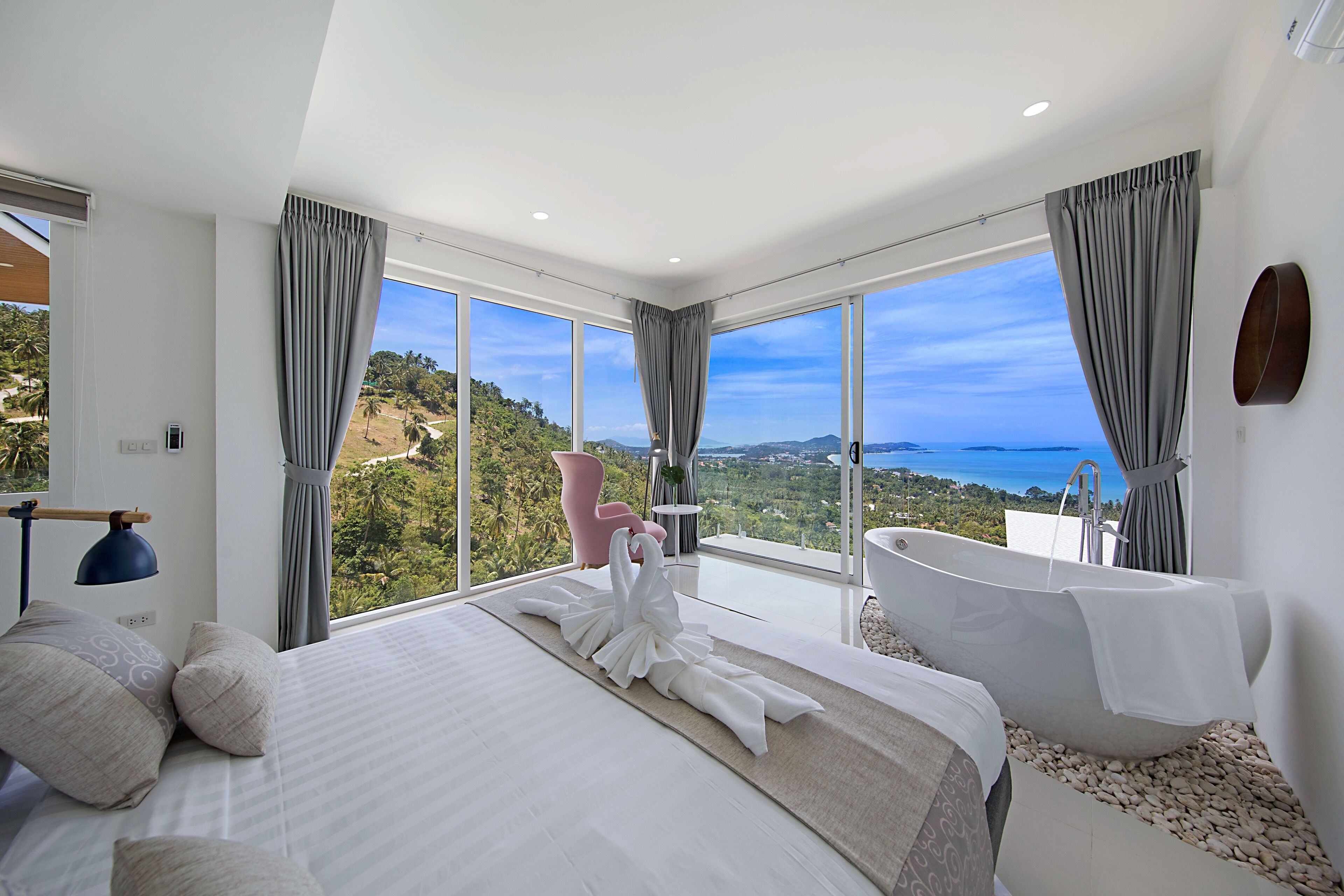 A bedroom with a large bed, a bathtub, and a view of the landscape.