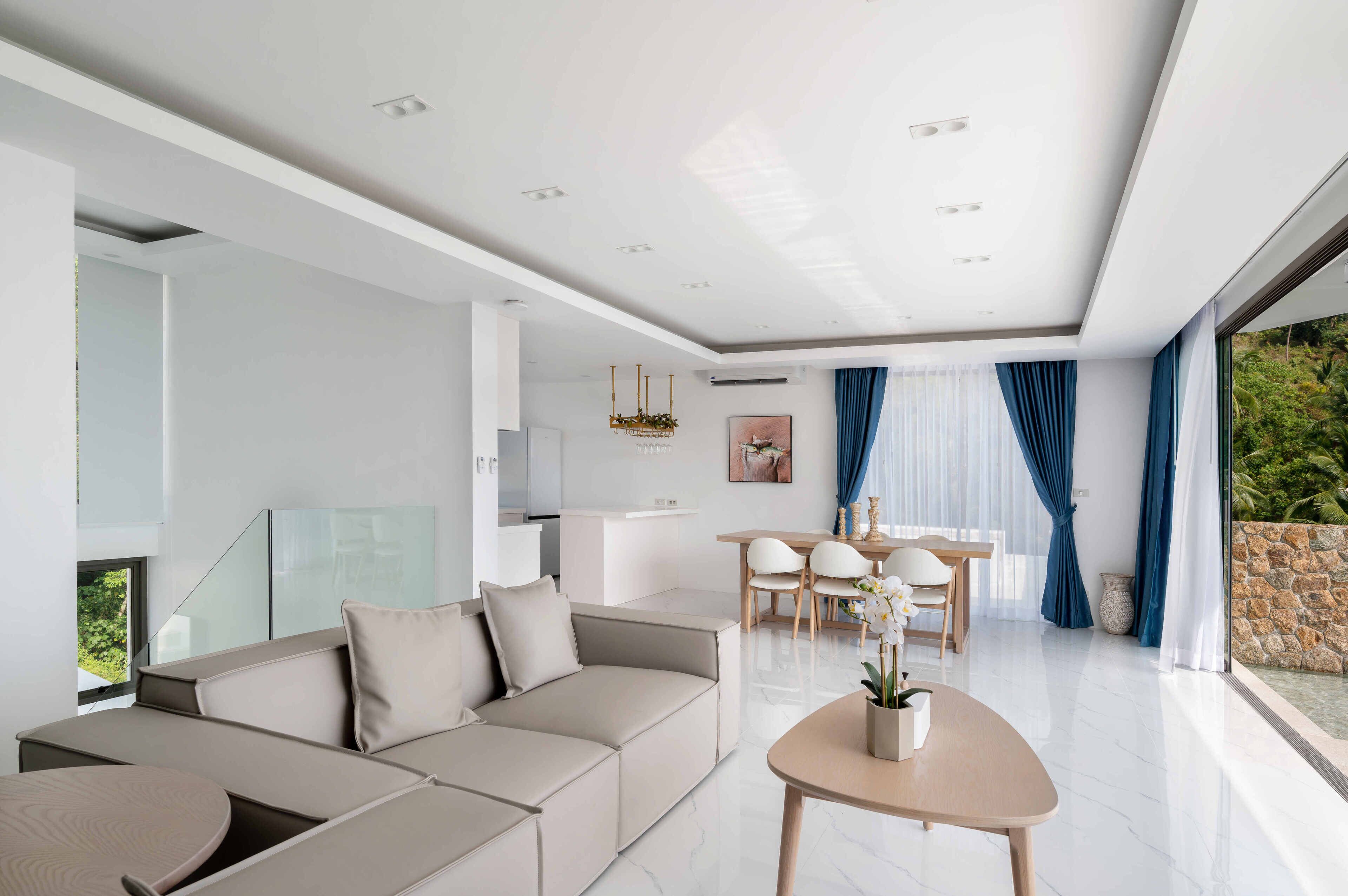 A modern living room with a sofa, a dining table with chairs, and a kitchen area in the background.