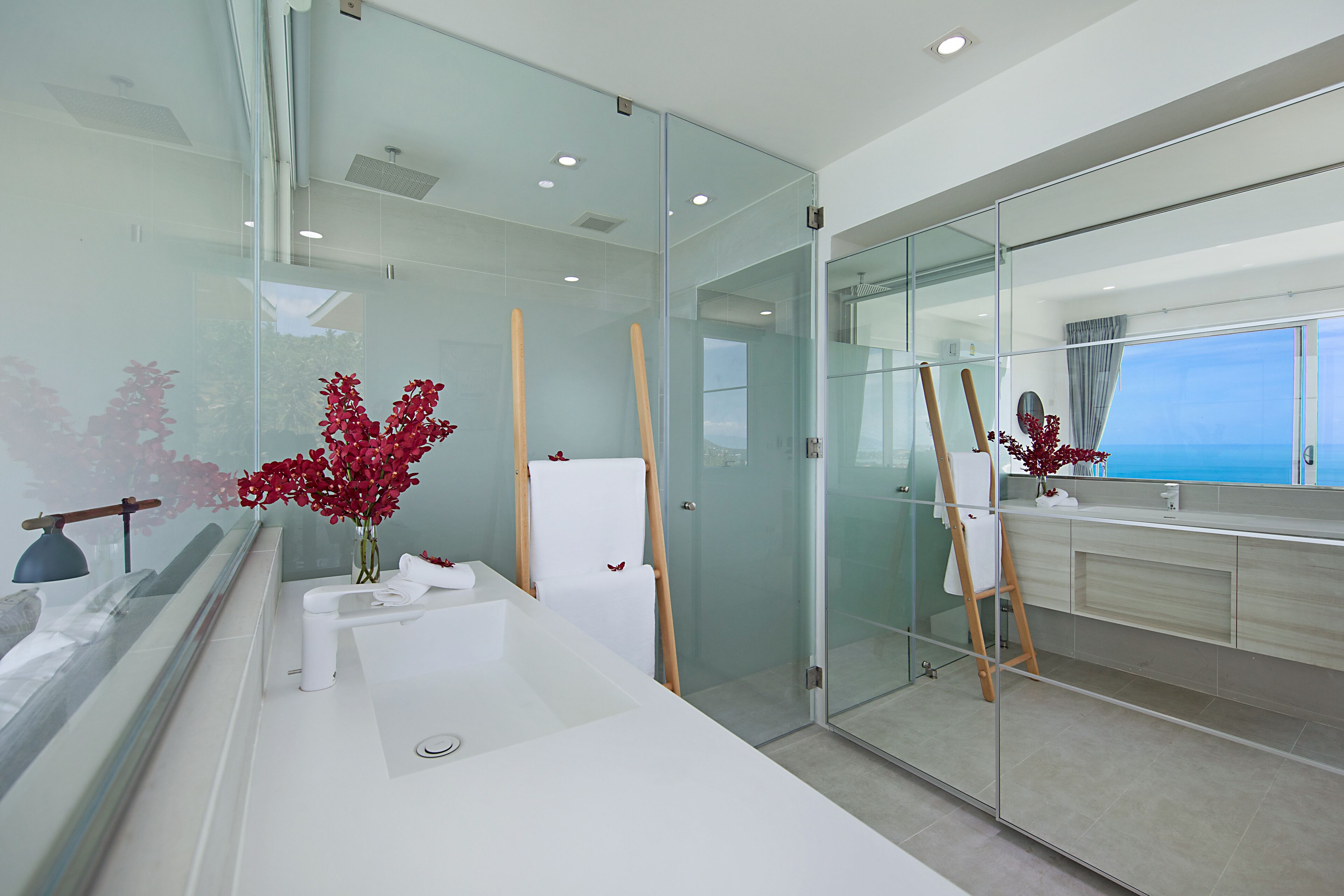 A modern bathroom with a glass shower enclosure, a white vanity, and a view of the ocean.